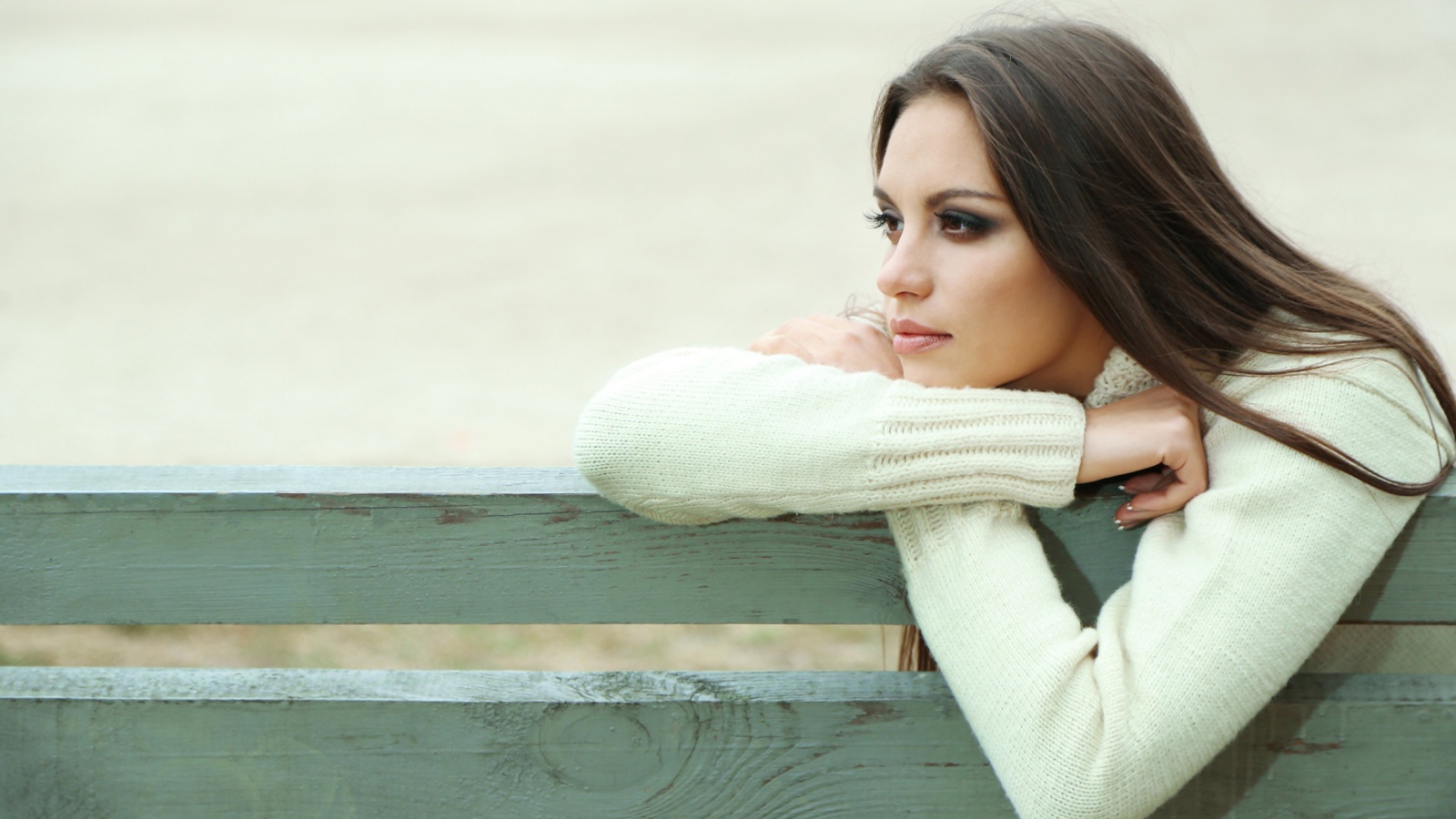 Задумчивая девушка брюнетка в белом свитере сидит на лавке