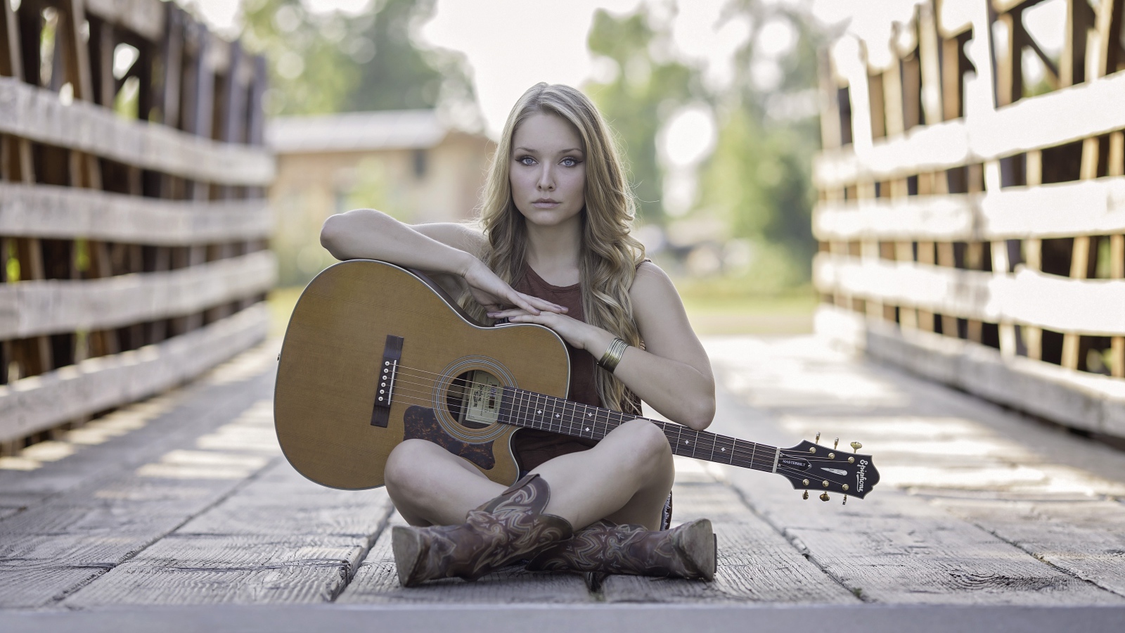 Молодая девушка блондинка сидит на мосту с гитарой