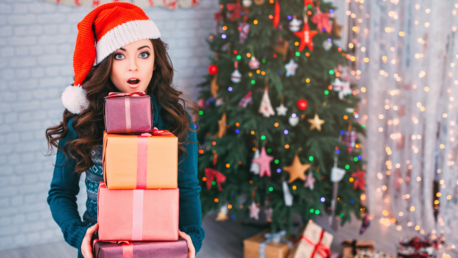 Удивленная девушка с подарками у новогодней елки 