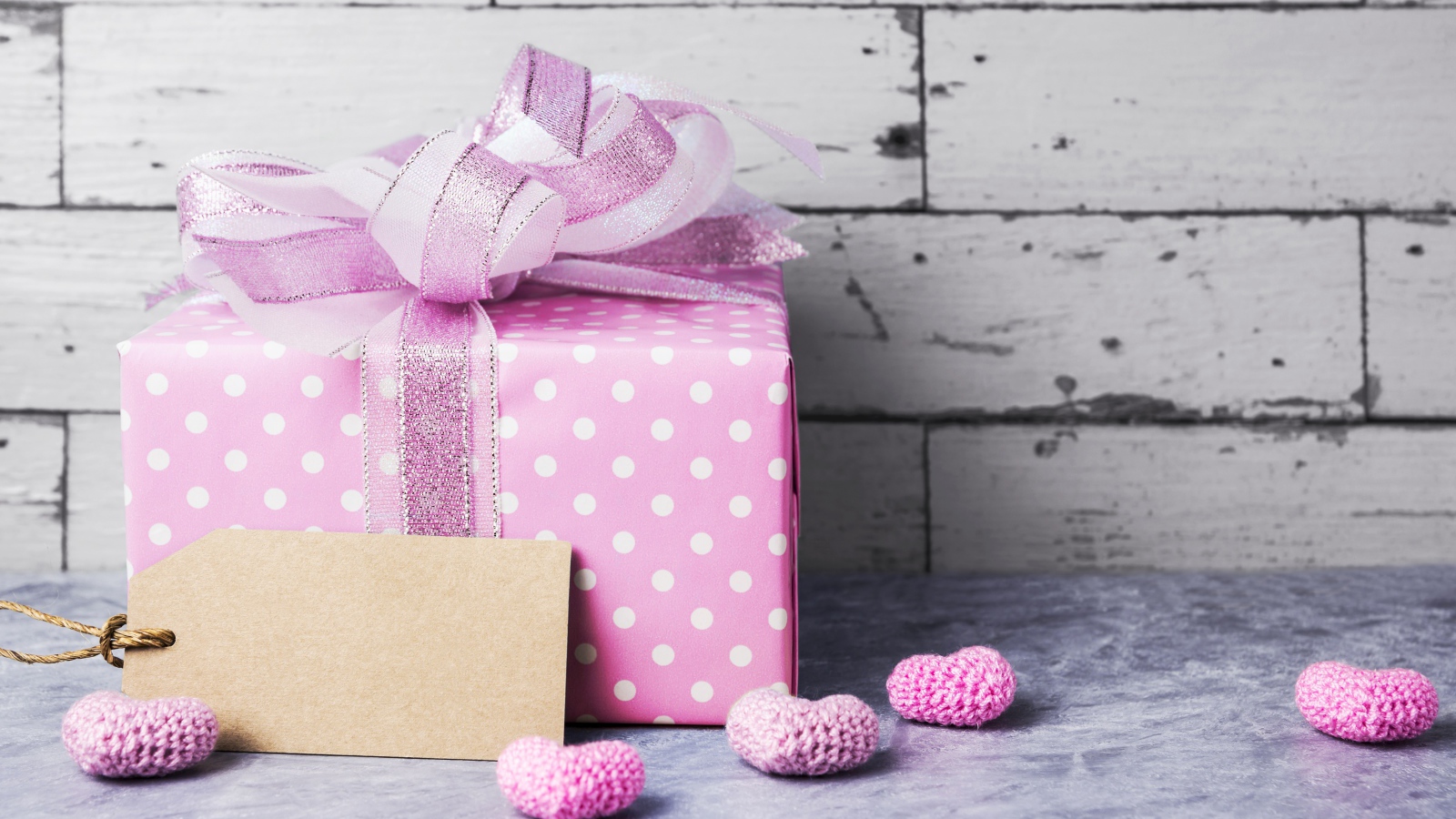 Большая сиреневая подарочная коробка с бантом и маленькими сердечками на фоне стены