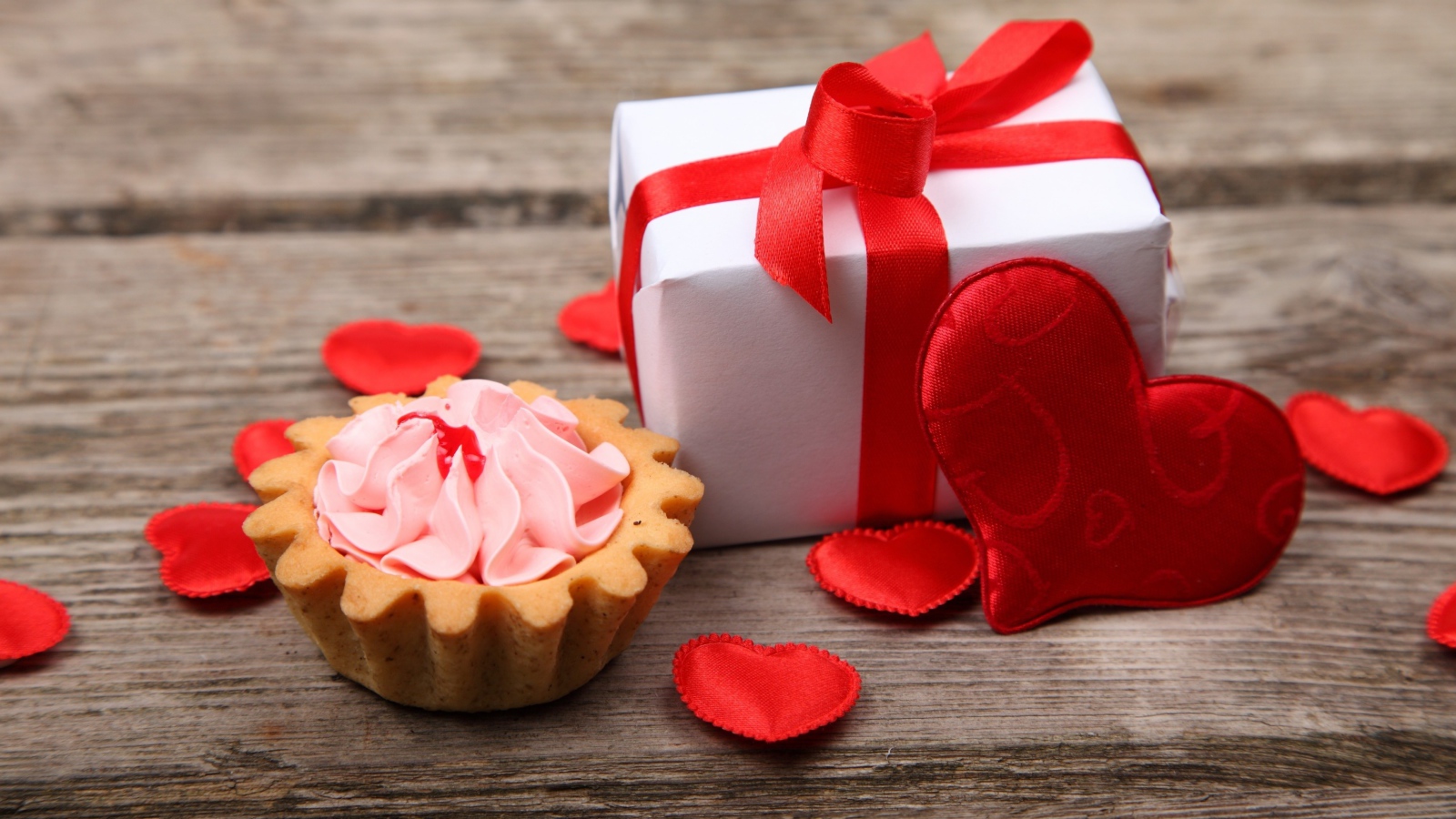 Пирожное, подарок и сердечки на деревянном фоне на День Святого Валентина
