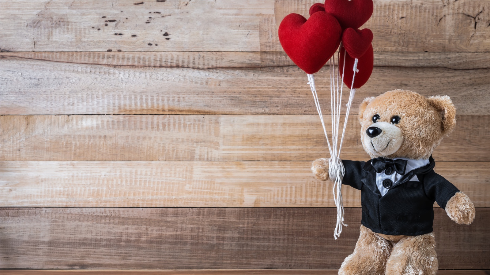 Плюшевый медведь с сердечками на деревянном фоне