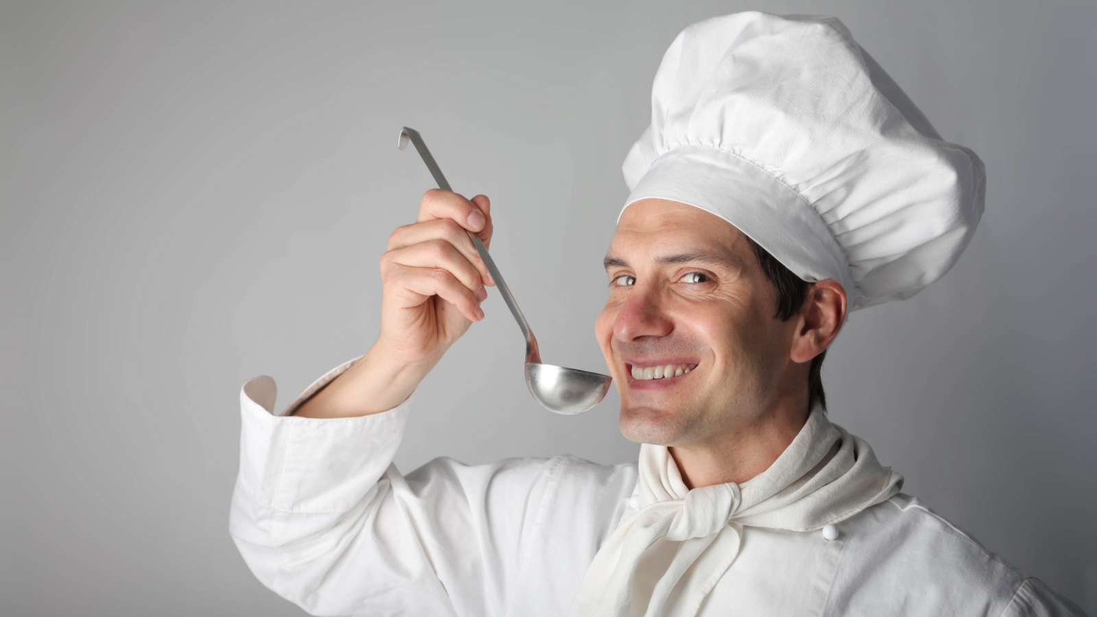 Улыбающийся мужчина повар с половником в руках на сером фоне