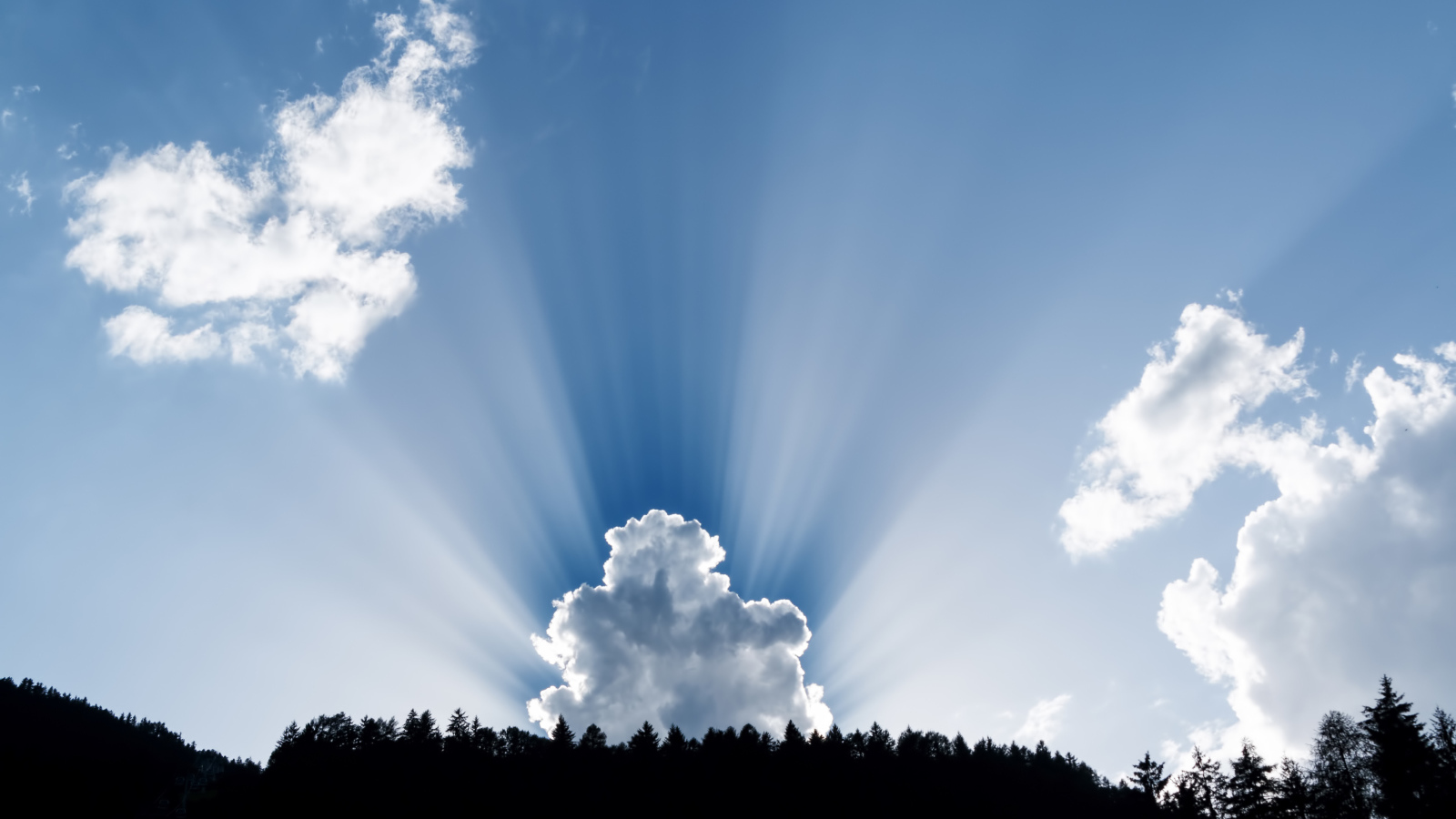 Лучи солнца пробиваются сквозь белые облака в голубом небе 