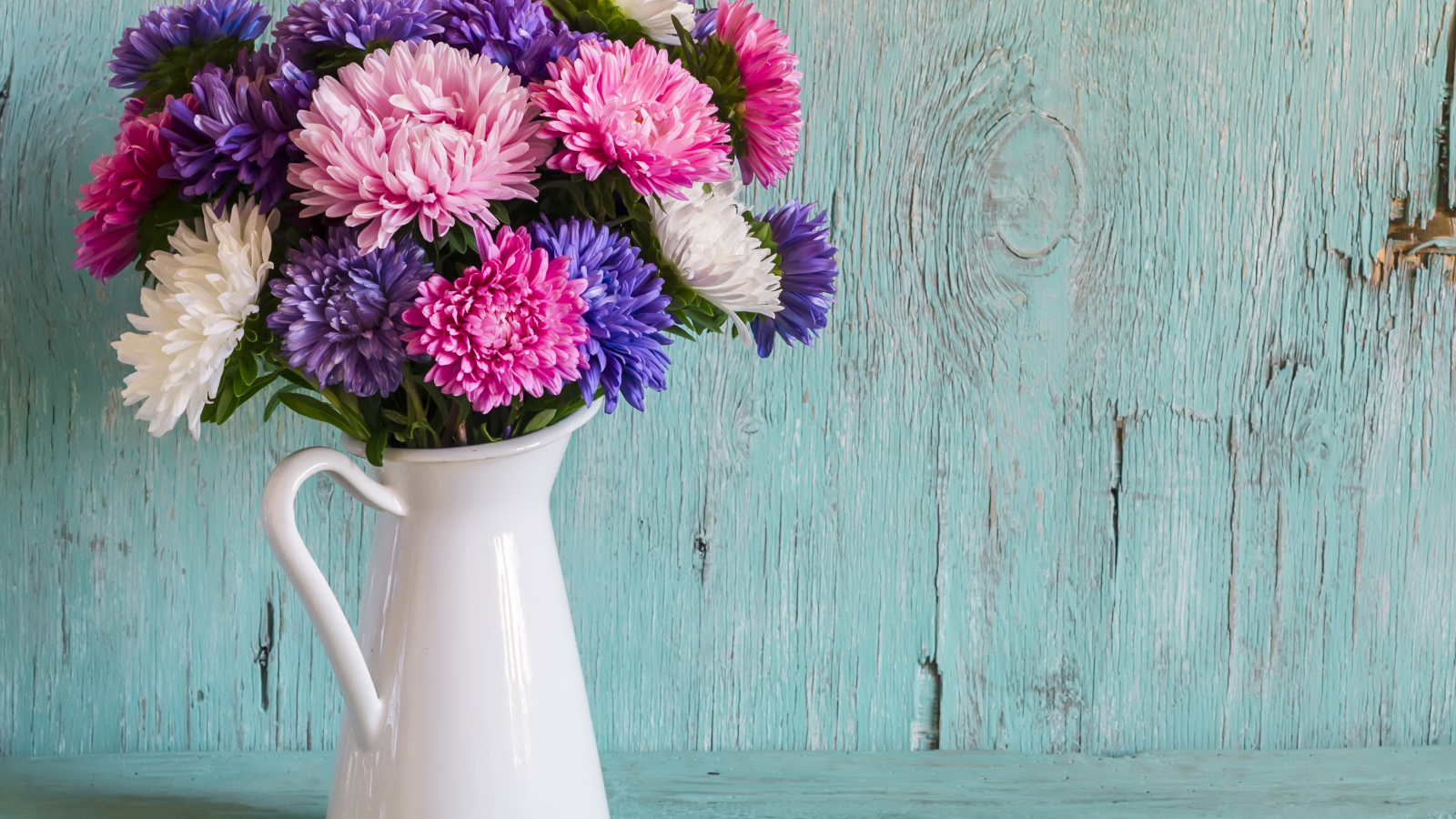 Разноцветные астры в вазе на деревянном фоне