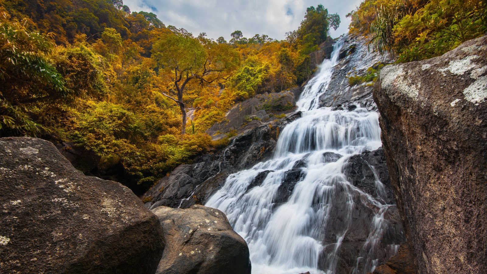Водопад стекает со скалы на фоне леса осенью