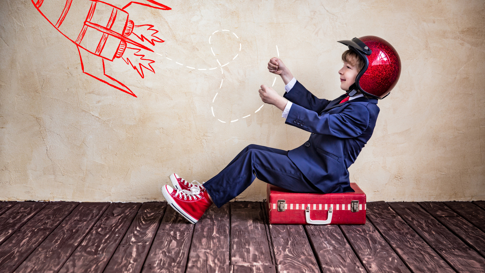 Маленький мальчик в шлеме сидит на чемодане