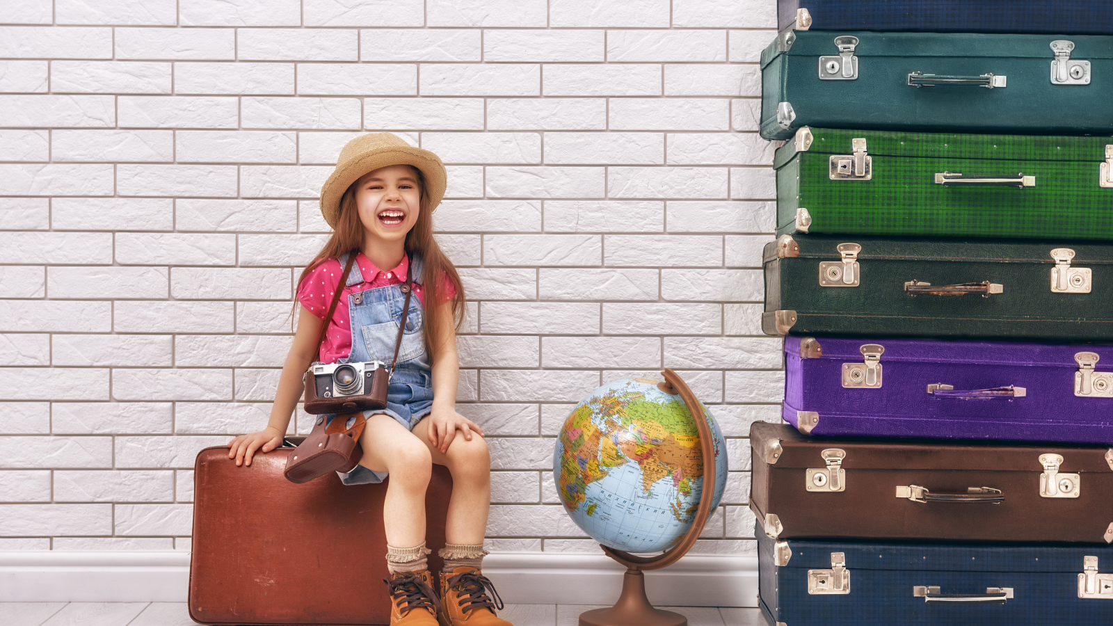 Маленькая девочка с фотоаппаратом сидит на чемодане