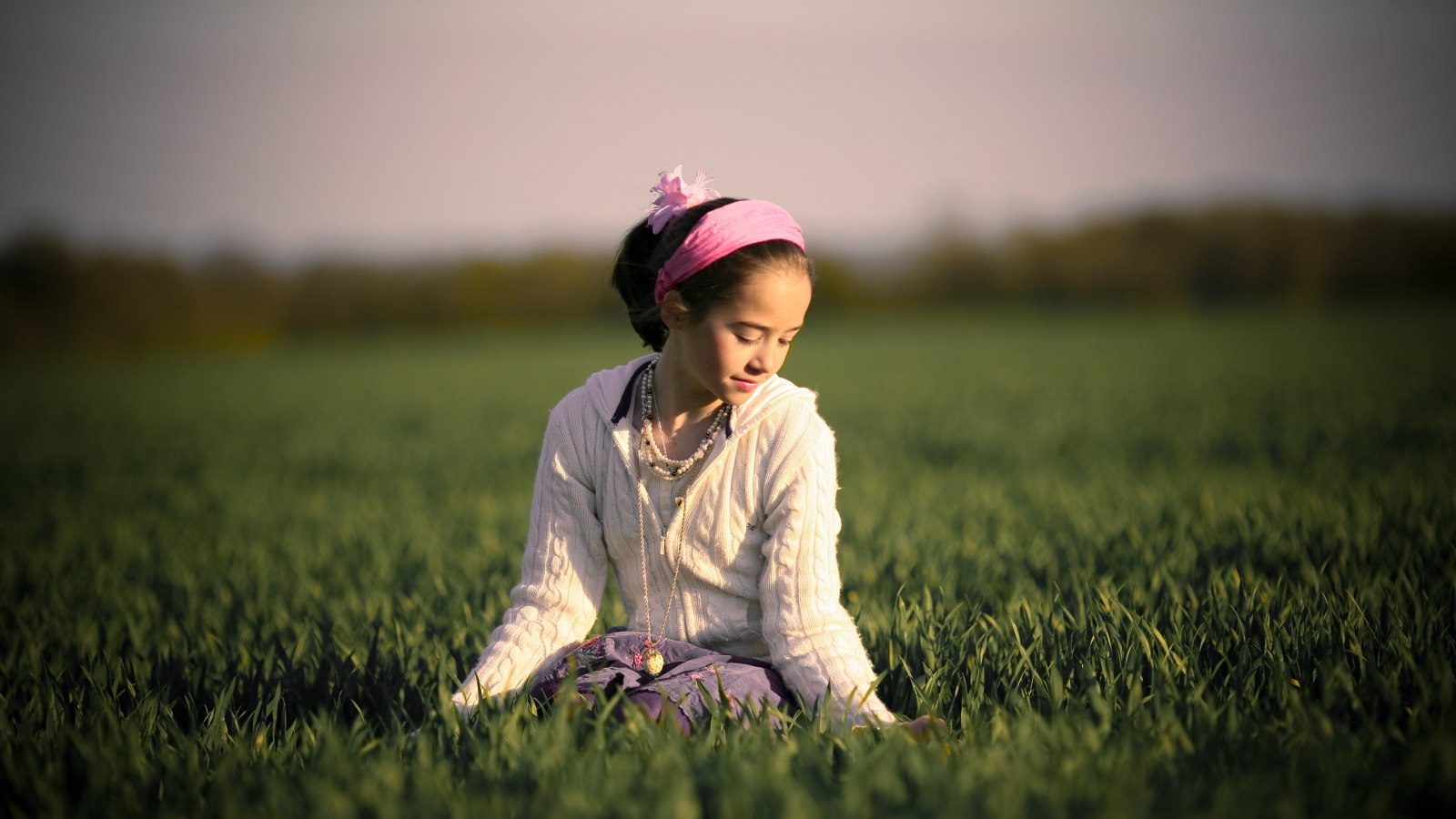 Девочка с розовой повязкой на голове сидит в зеленой траве