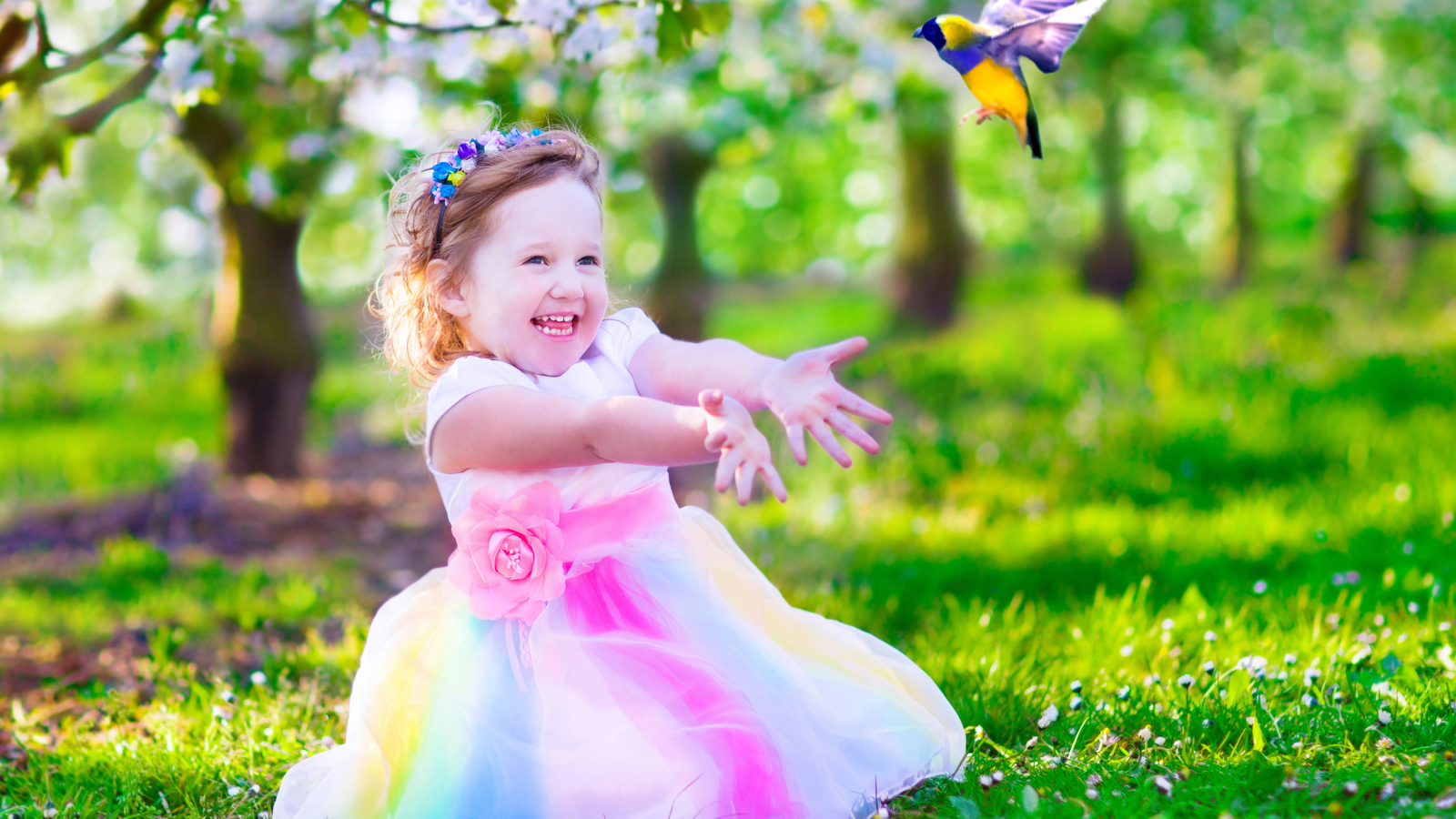 Смеющаяся маленькая девочка в красивом платье на зеленой траве