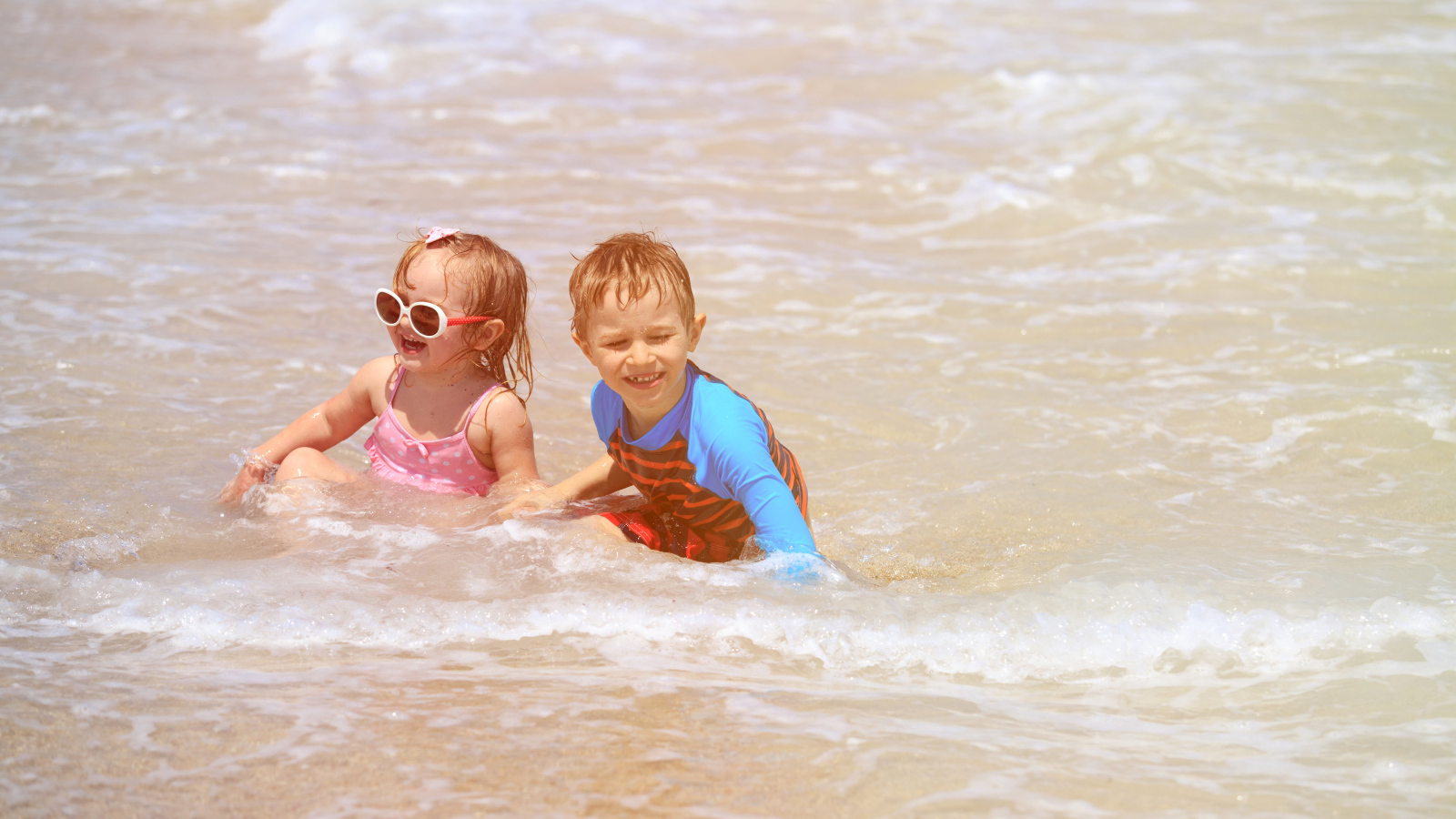 Маленькие мальчик и девочка купаются в море 