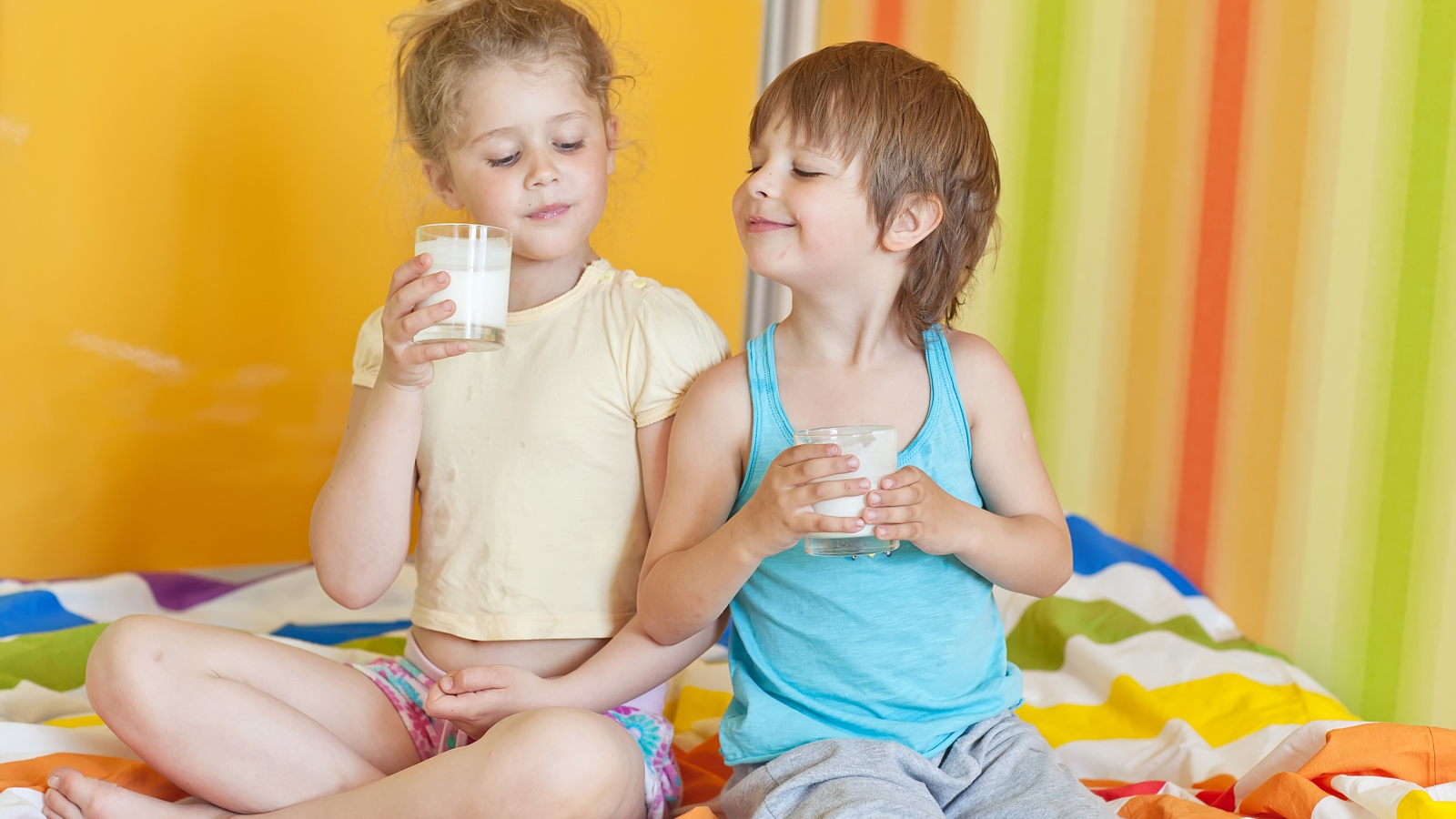 Маленькие мальчик и девочка со стаканами молока в руках 