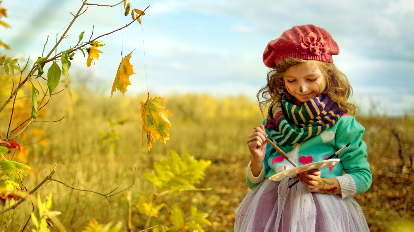 Маленькая девочка рисует красками на листьях осенью 