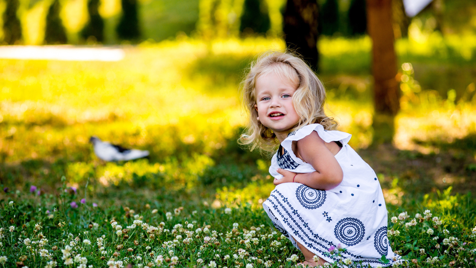 Маленькая девочка в красивом платье сидит на зеленой траве