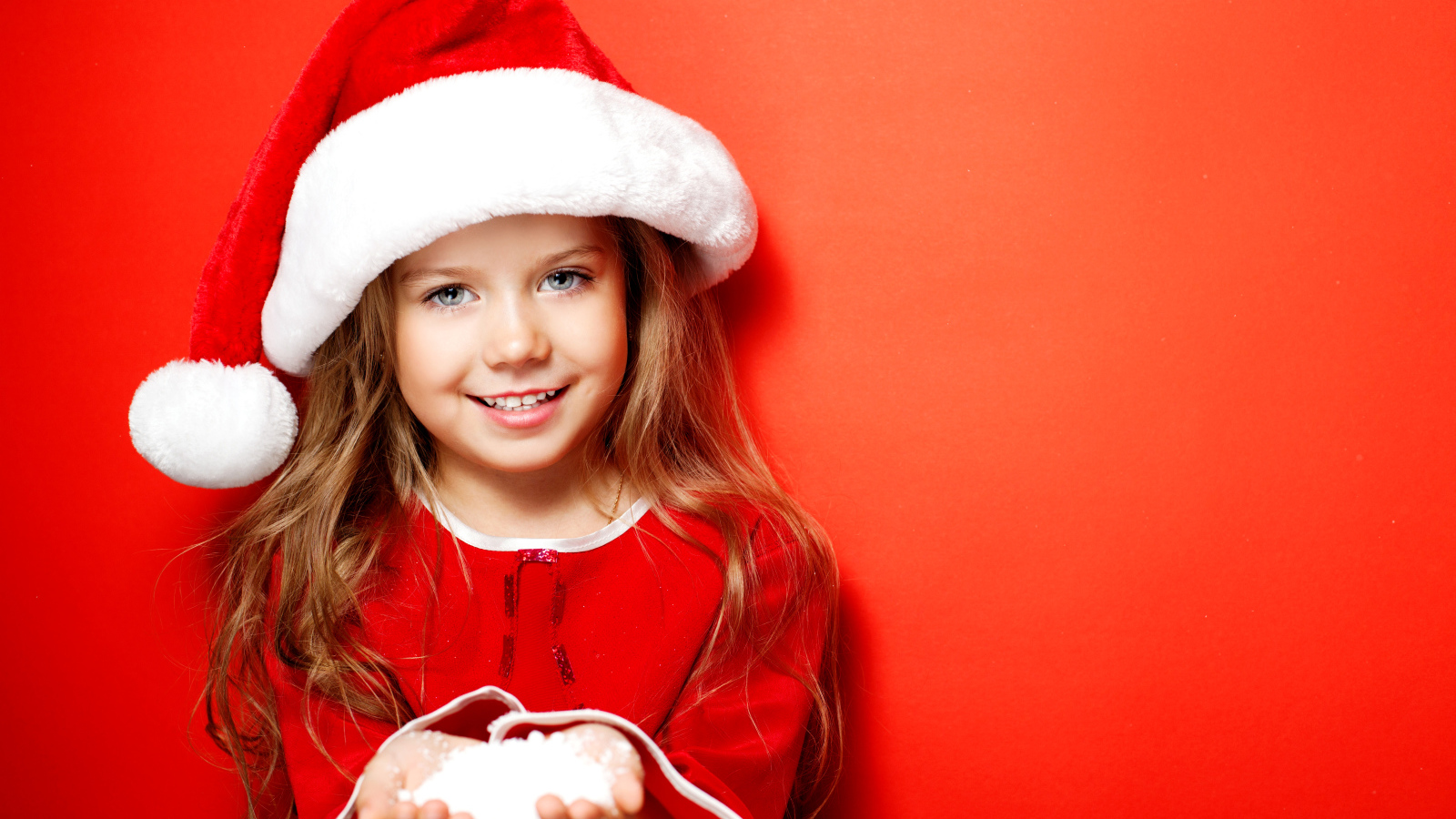 Маленькая девочка в новогодней шапке на красном фоне