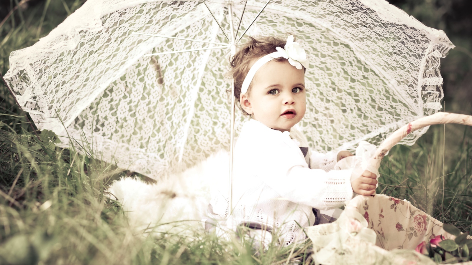 Маленькая девочка сидит на траве с большим белым зонтом