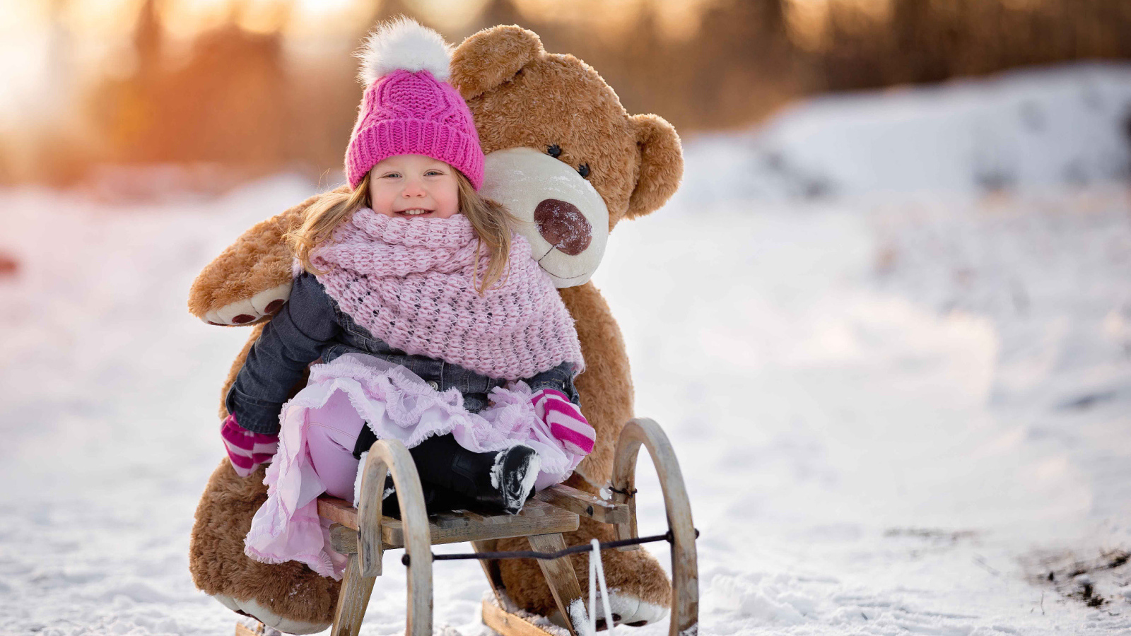 Маленькая девочка на санках с большим медведем зимой 