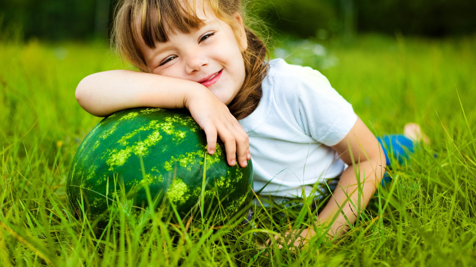 Улыбающаяся девочка с зеленым арбузом на траве