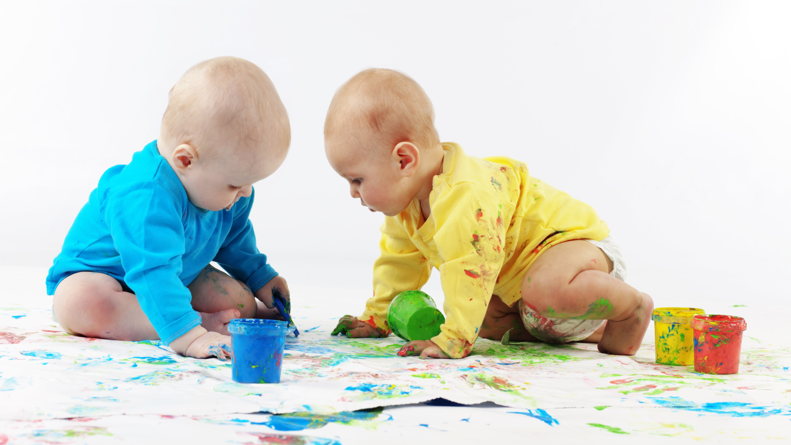Два малыша рисуют красками на белом фоне