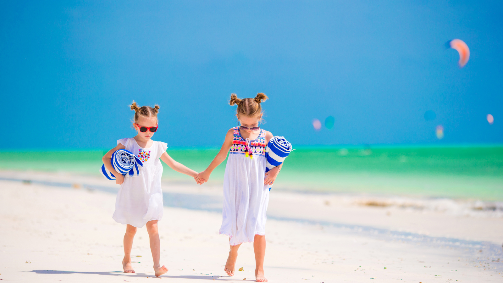 Две маленькие девочки идут по песку