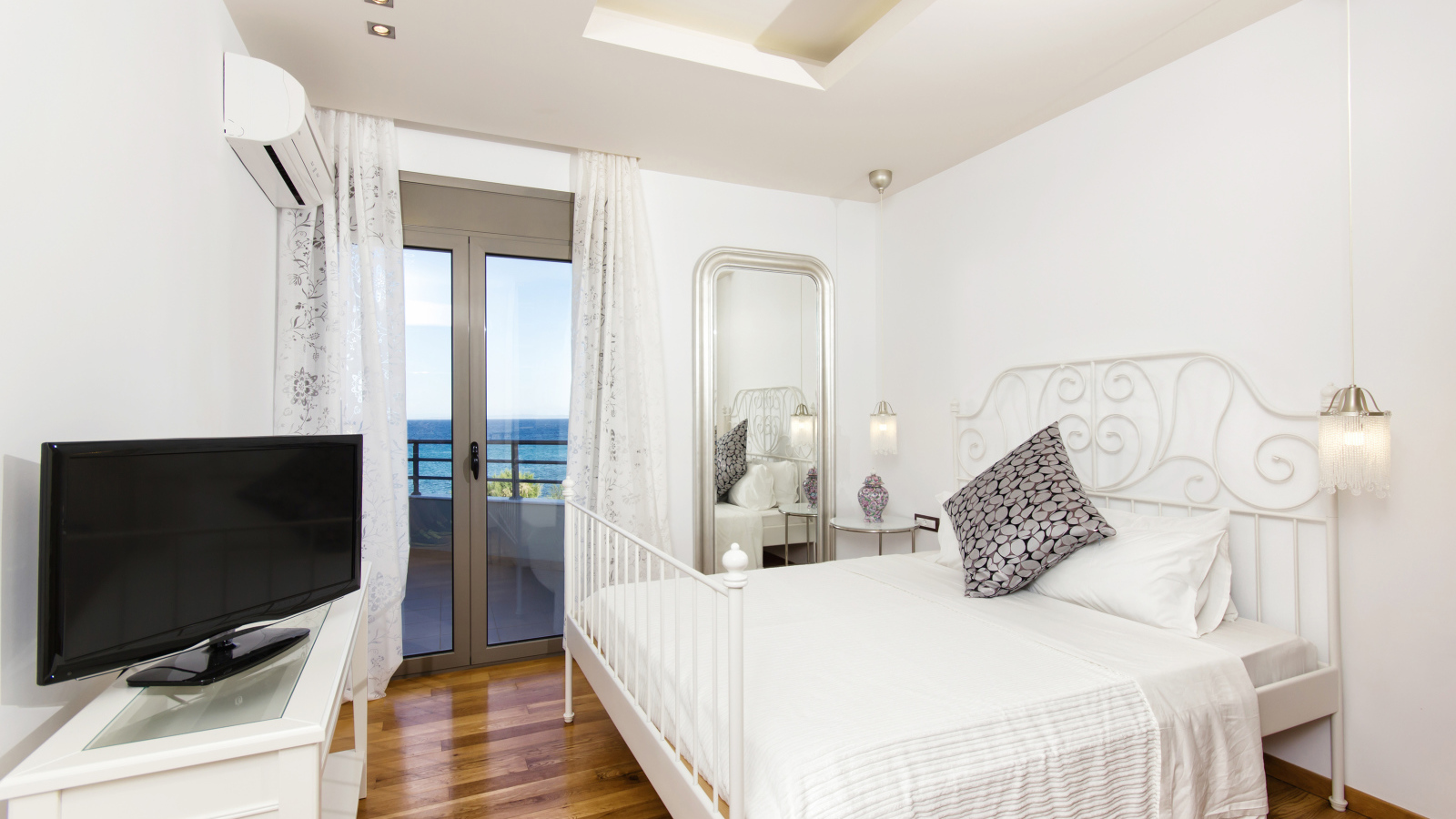 Светлая спальня с большой белой кроватью и телевизором 