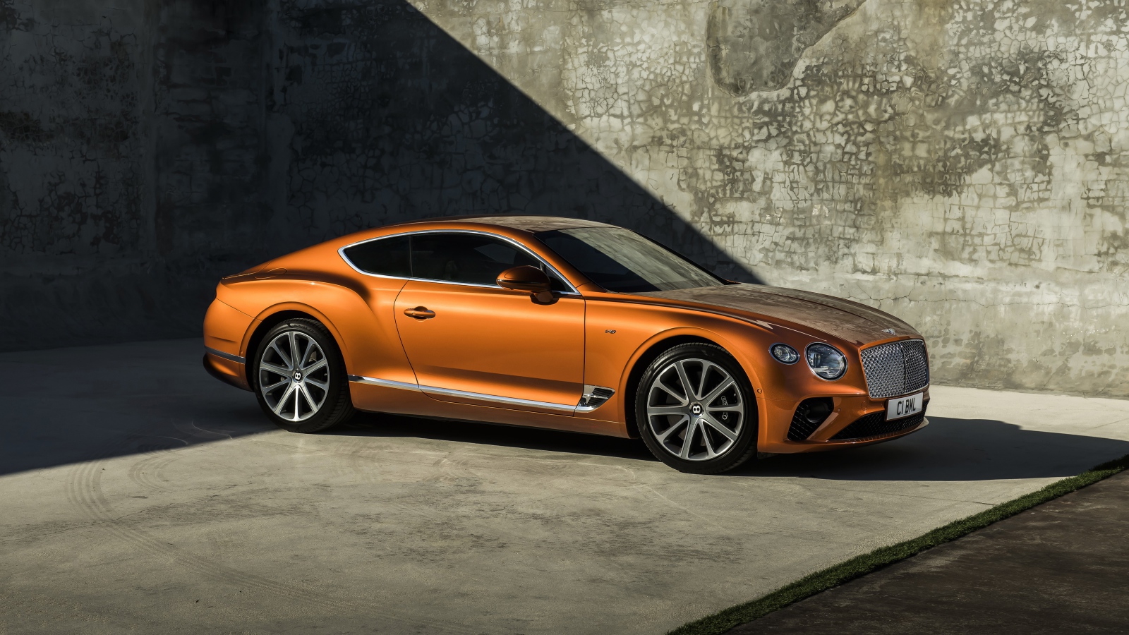 Оранжевый автомобиль Bentley Continental GT V8, 2019 года на фоне стены