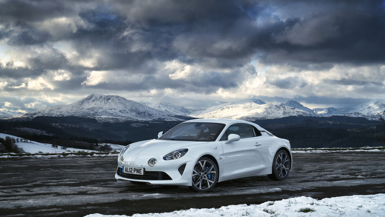 White car Alpine A110 on a background of mountains under a stormy sky