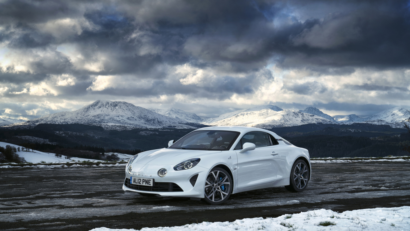 Белый автомобиль Alpine A110 на фоне гор под грозовым небом  