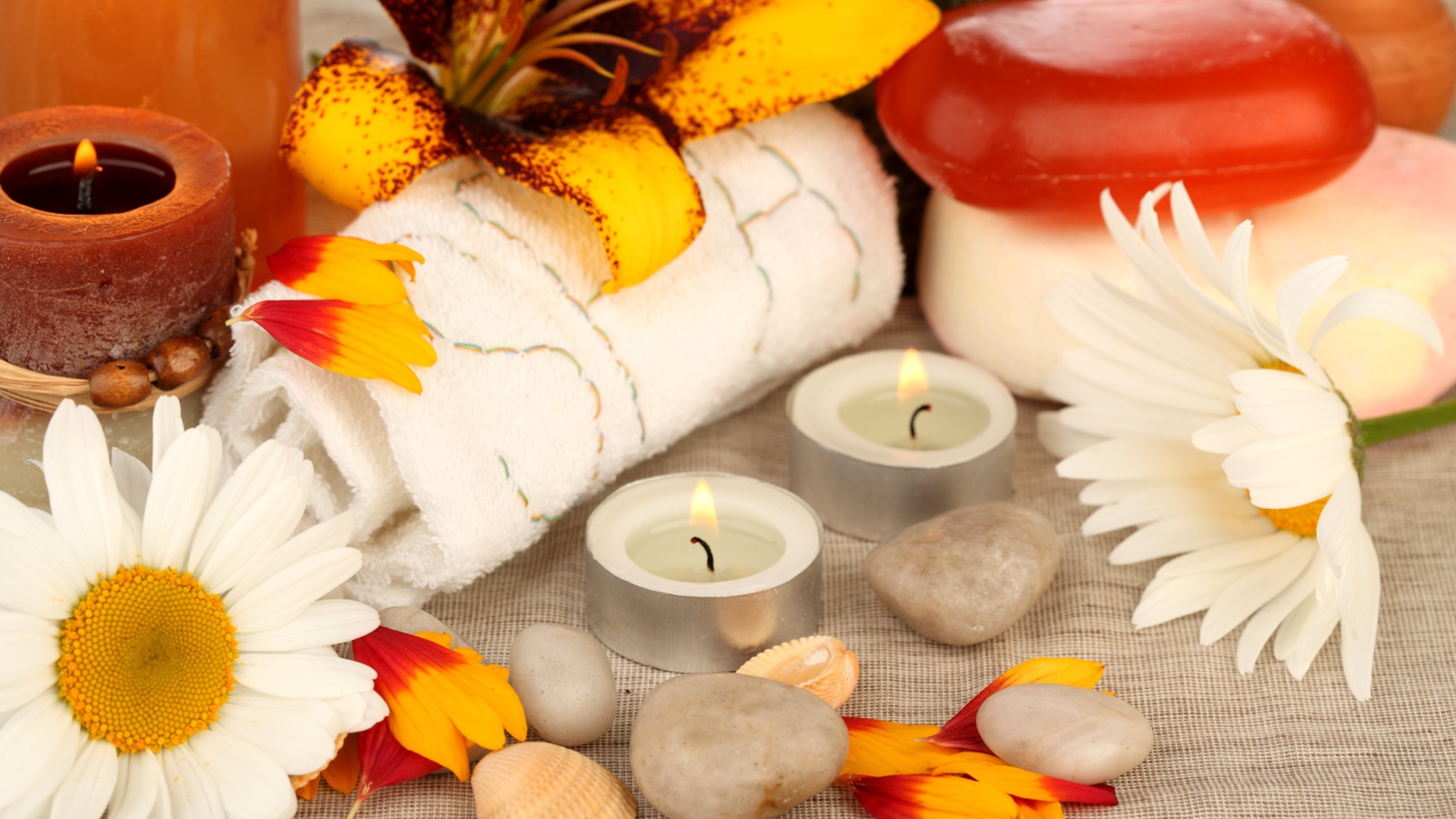 Зажженные свечи на столе с полотенцем, цветами и мылом