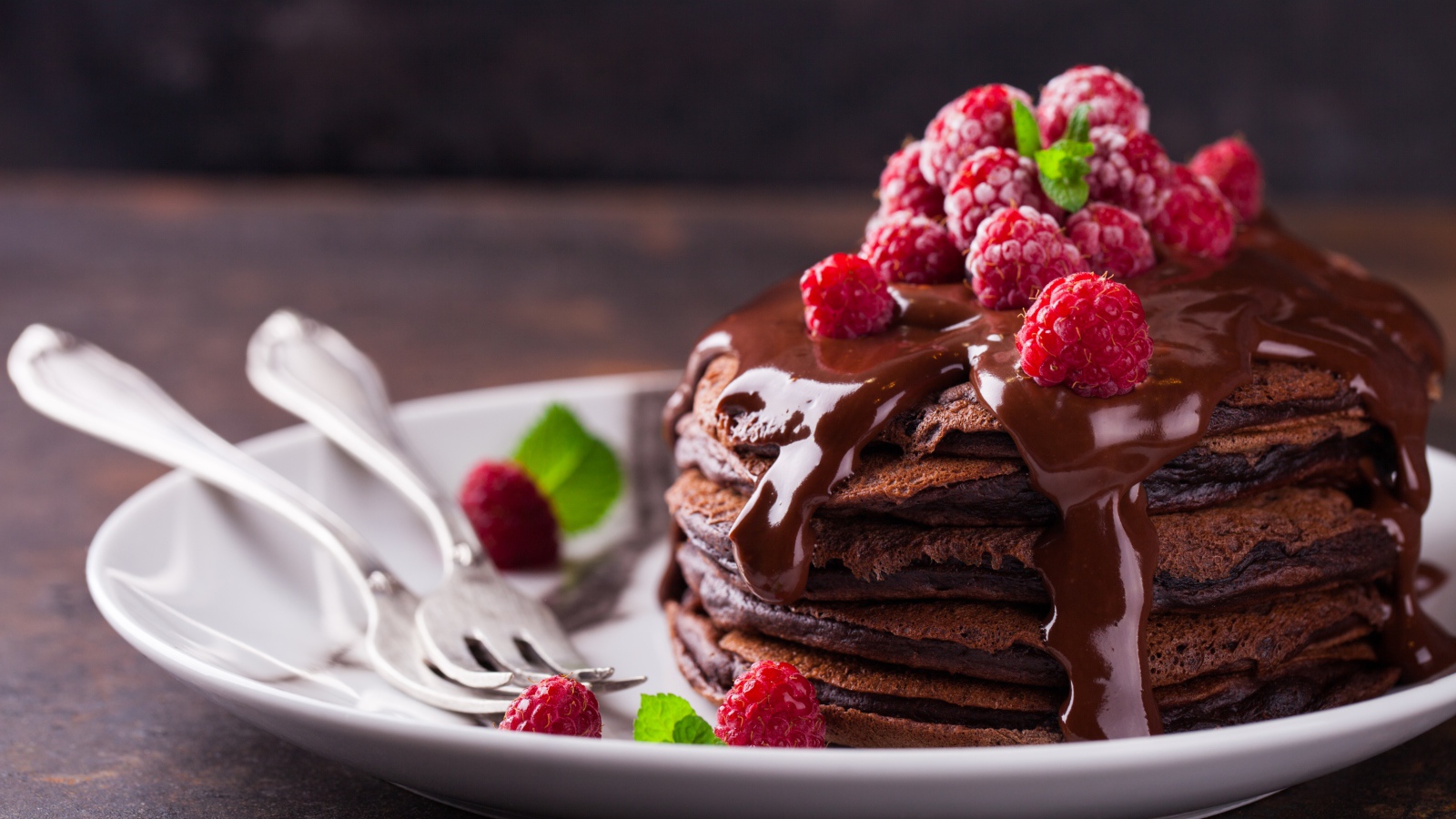 Шоколадные оладьи на тарелке с шоколадом и ягодами малины 