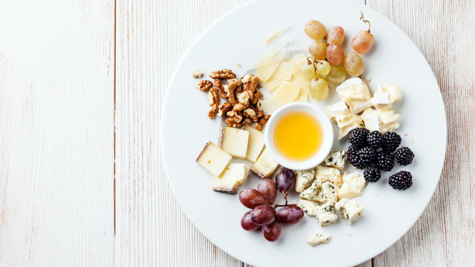 Куски сыра на тарелке с орехами, виноградом, медом и ягодами ежевики