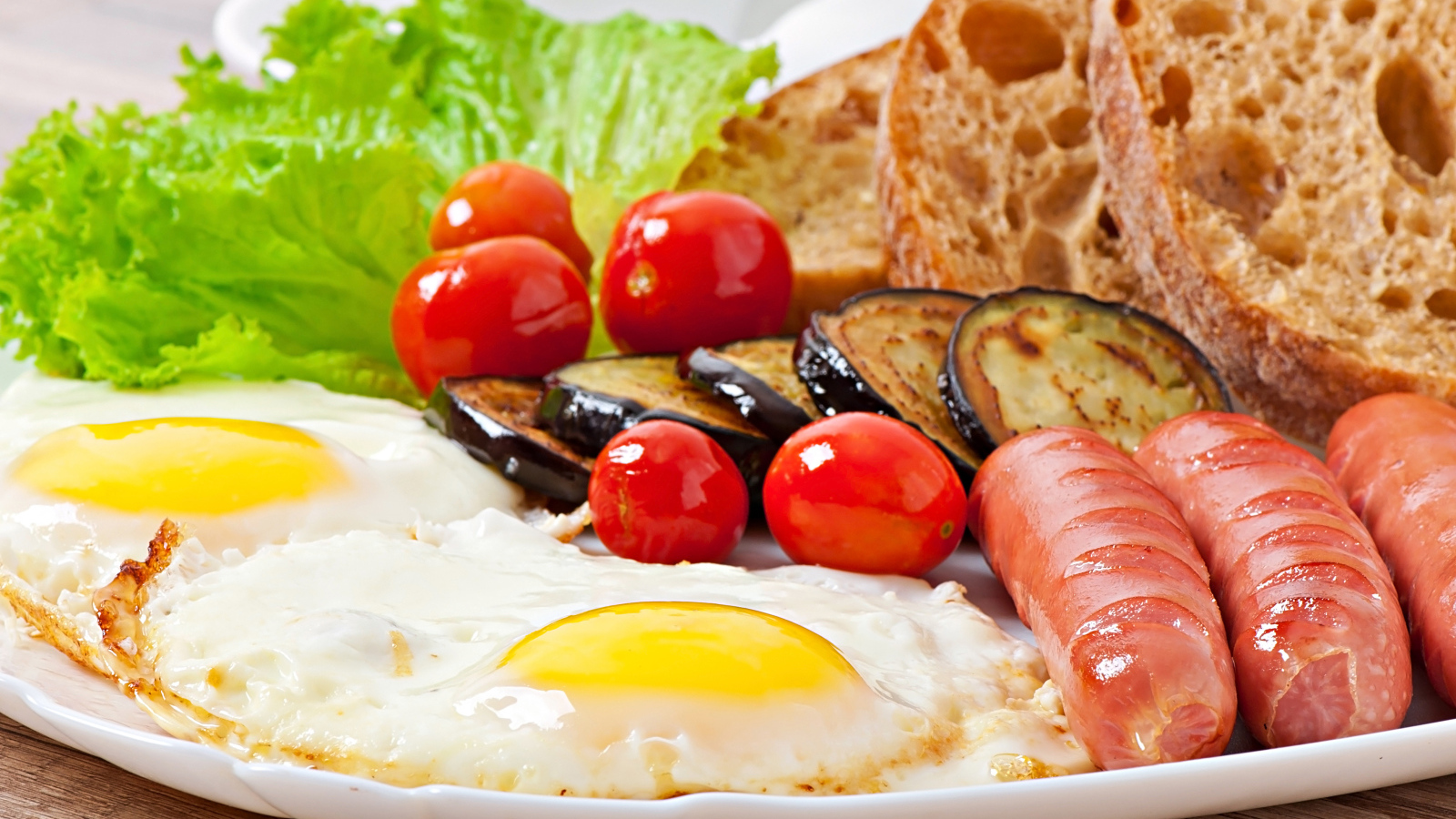 Яичница на тарелке с сосисками, овощами и хлебом