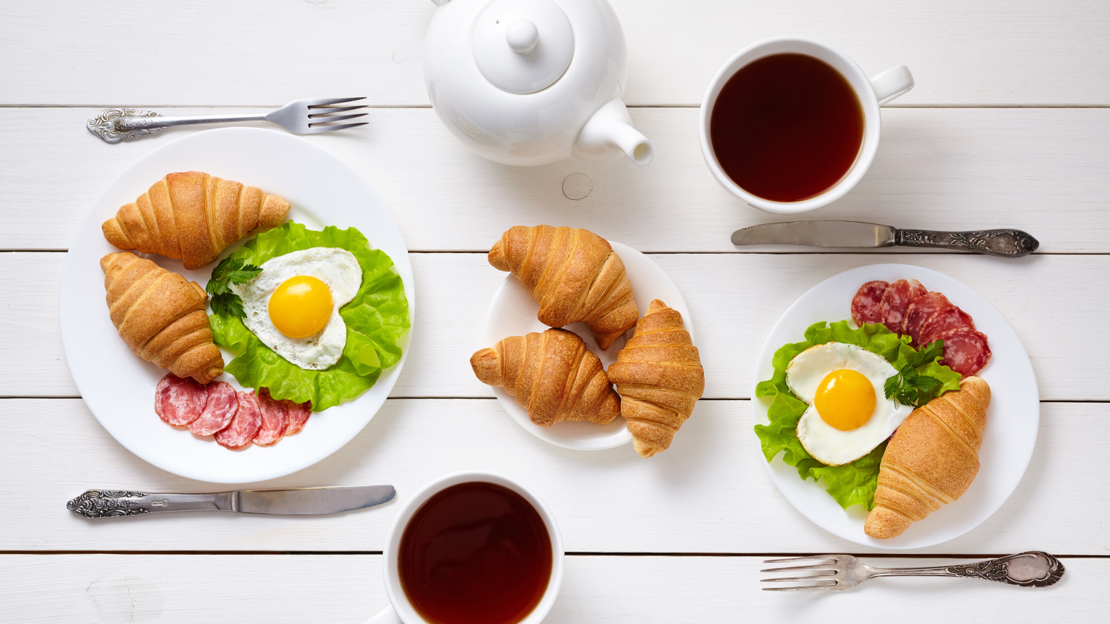 Яичница с колбасой и круассанами на столе чаем 