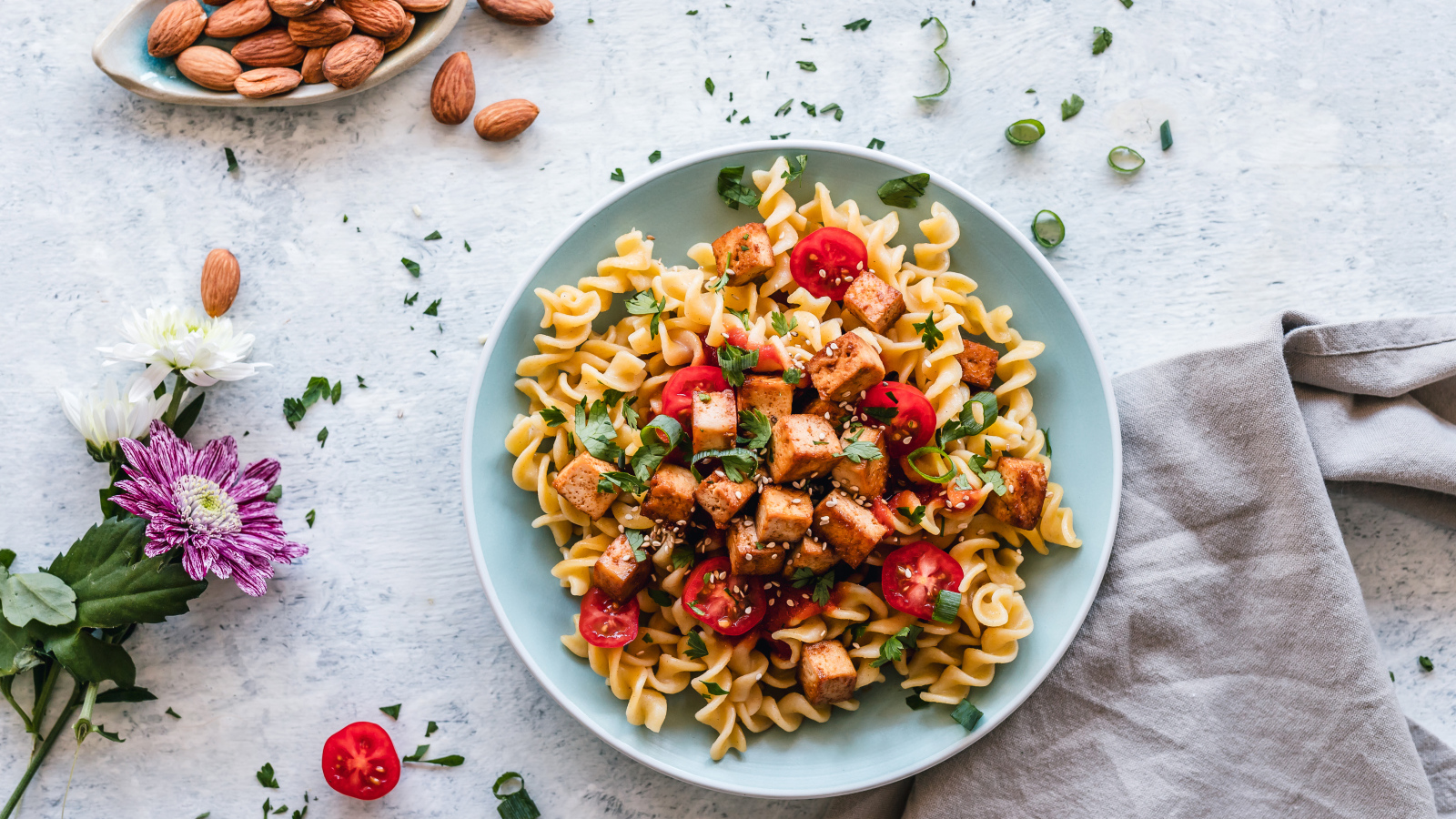 Макароны с мясом и овощами на столе с миндальными орехами