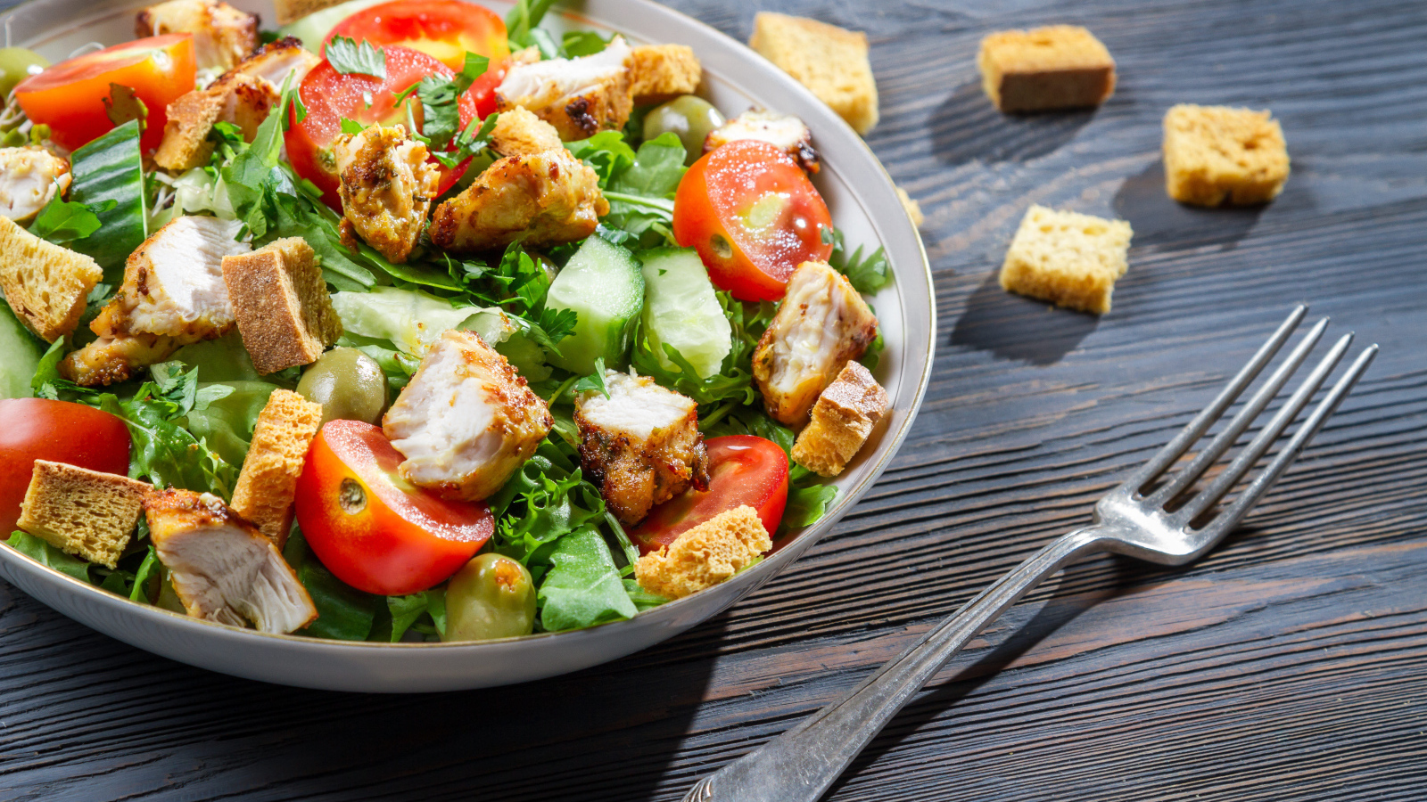 Салат с овощами, сухариками и курицей и на столе с вилкой