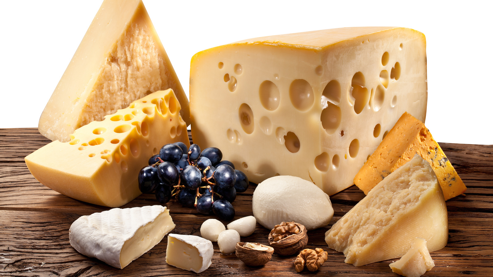 Куски сыра на деревянном столе с виноградом и грецким орехом