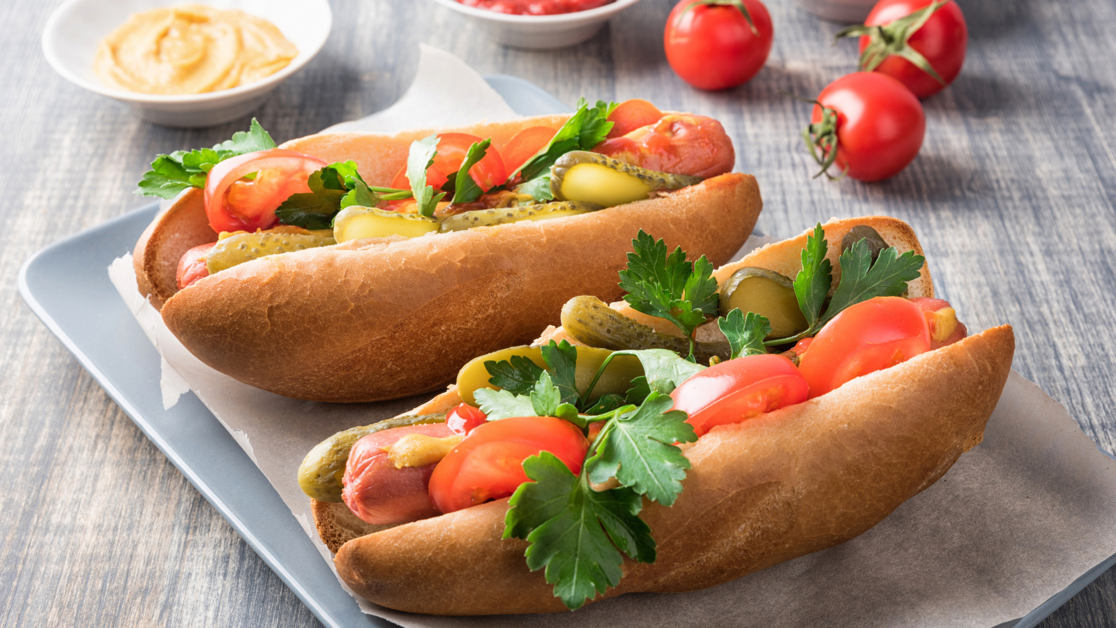 Two hotdogs with sausage, cucumbers and tomatoes