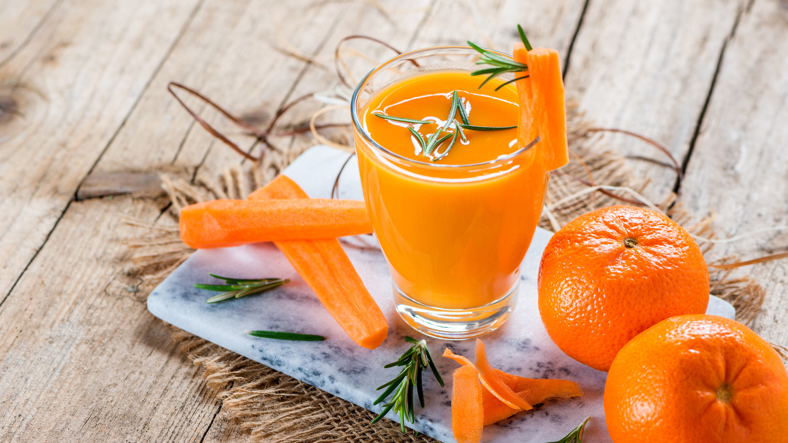 Два апельсина на столе со стаканом морковного сока