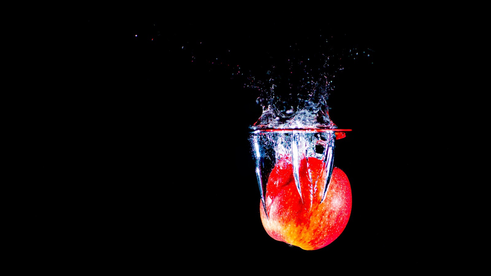 Красное яблоко падает в воду на черном фоне