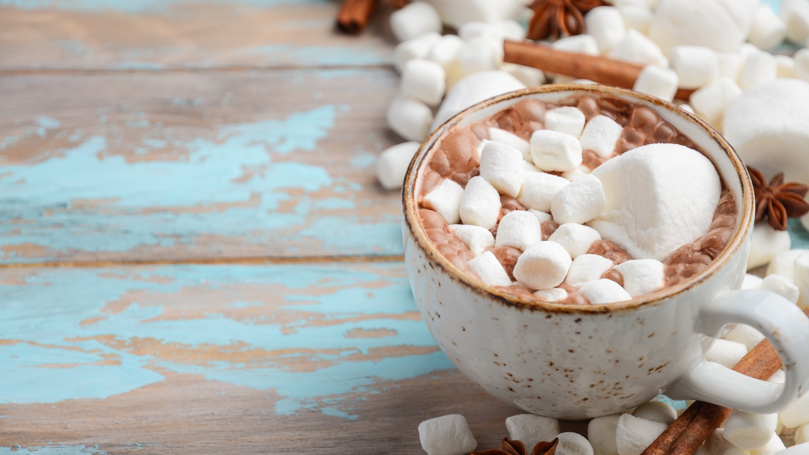 Чашка какао с маршмеллоу на столе с корицей и сладостями