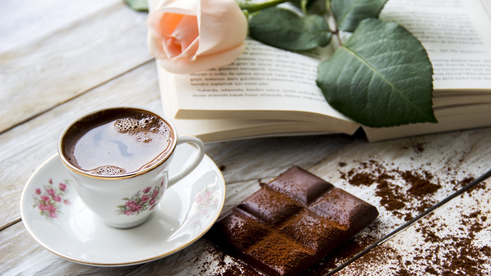 Чашка кофе на столе с шоколадом, книгой и розой