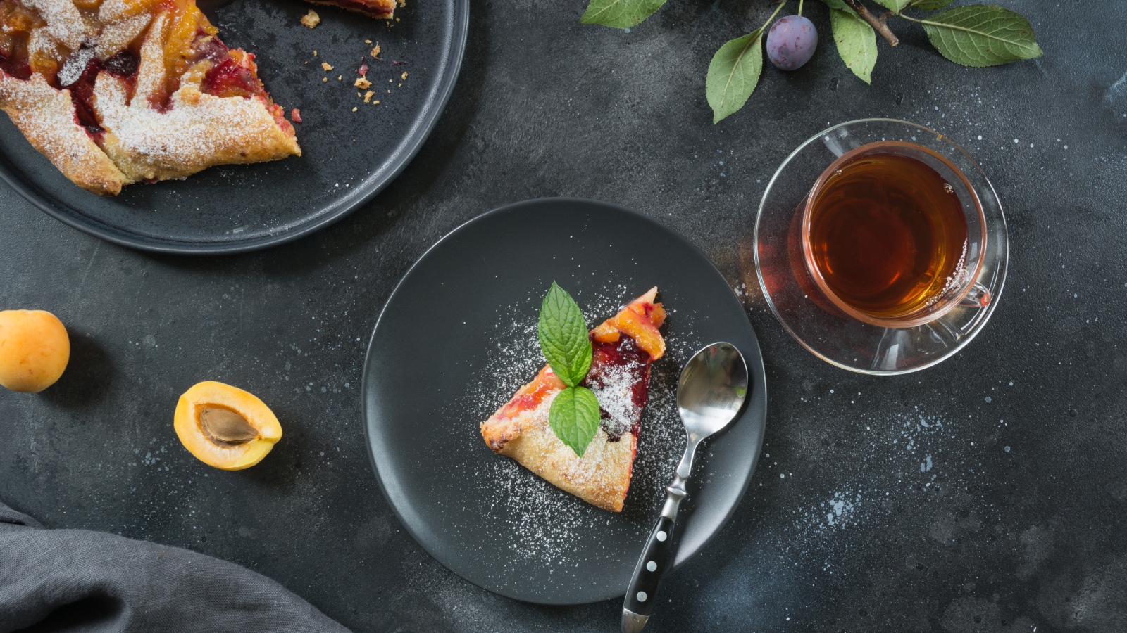 Кусок пирога с сахарной пудрой и абрикосами и сливами на столе с чаем 