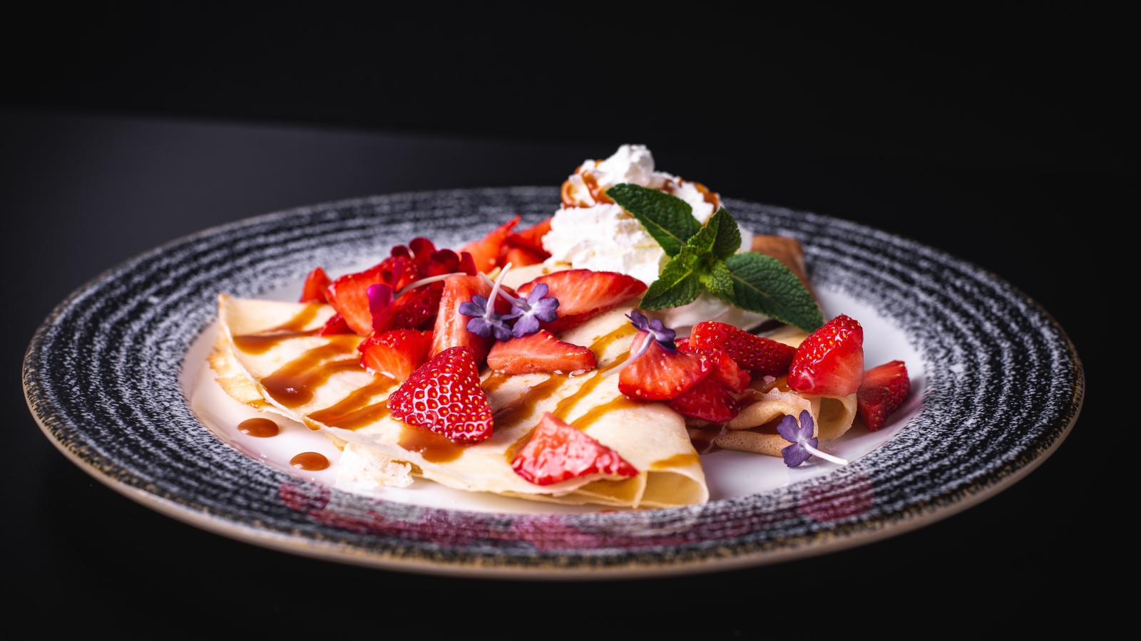 Аппетитные тонкие блинчики с клубникой на черном фоне