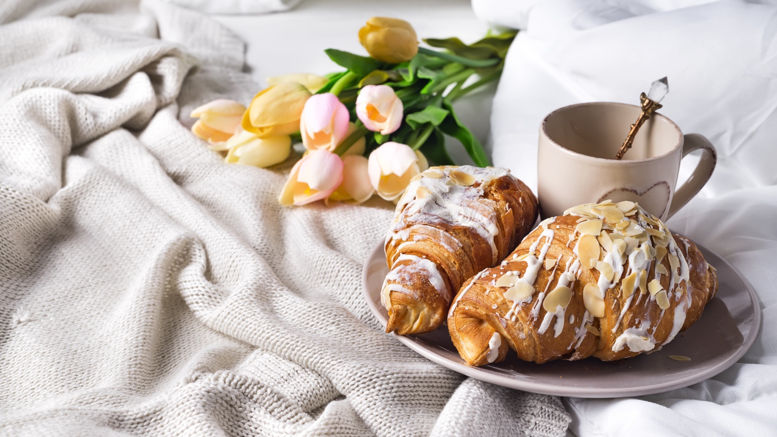 Круассаны на кровати с кофе и букетом тюльпанов