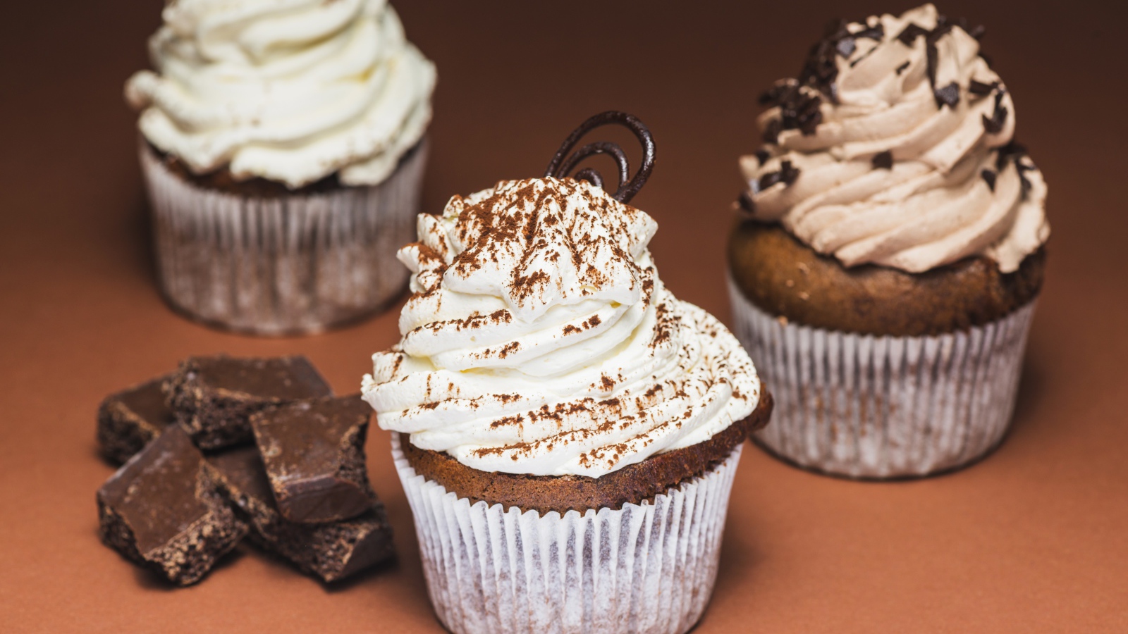 Кексы с кремом на столе с кусочками шоколада 