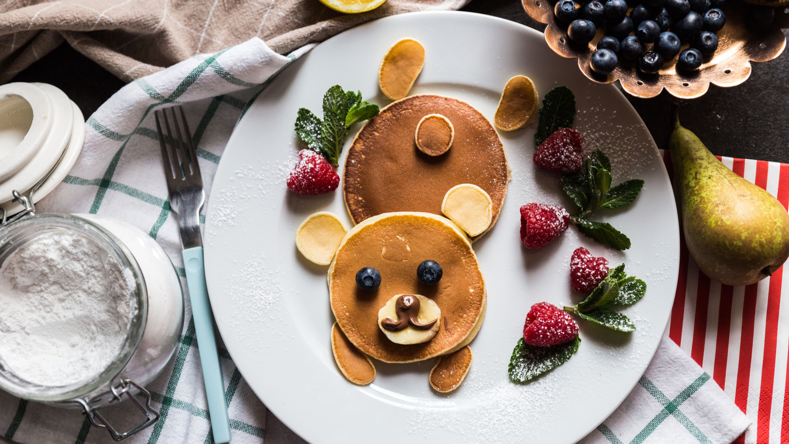 Медведь из оладьев на тарелке с малиной и сахарной пудрой