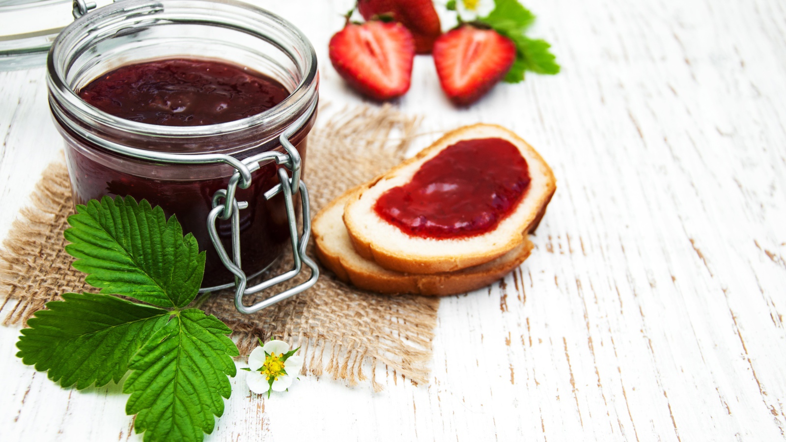 Банка клубничного джема на столе с батоном