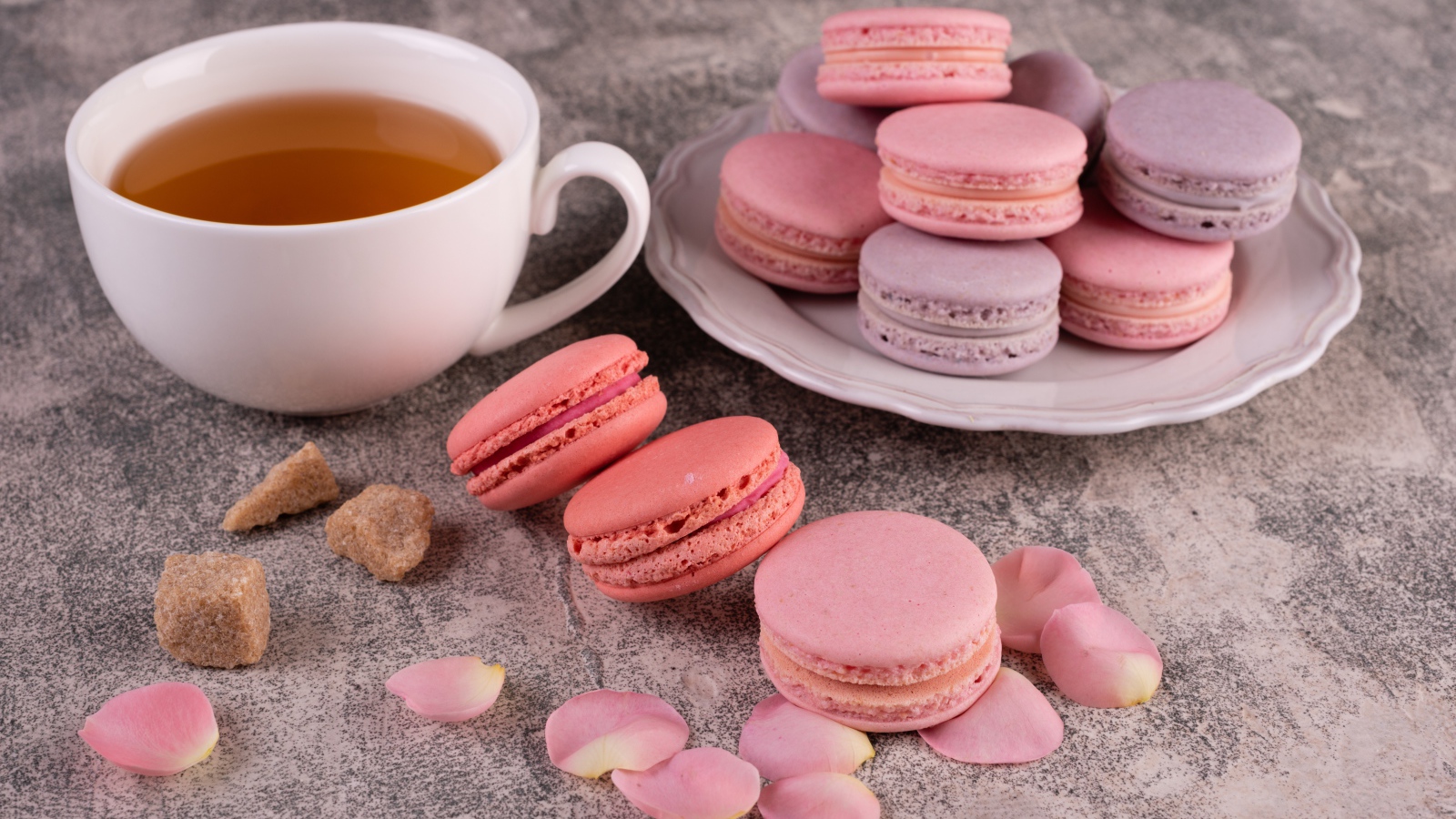 Сладкий десерт макарун на столе с чашкой чая, сахаром и лепестками розы