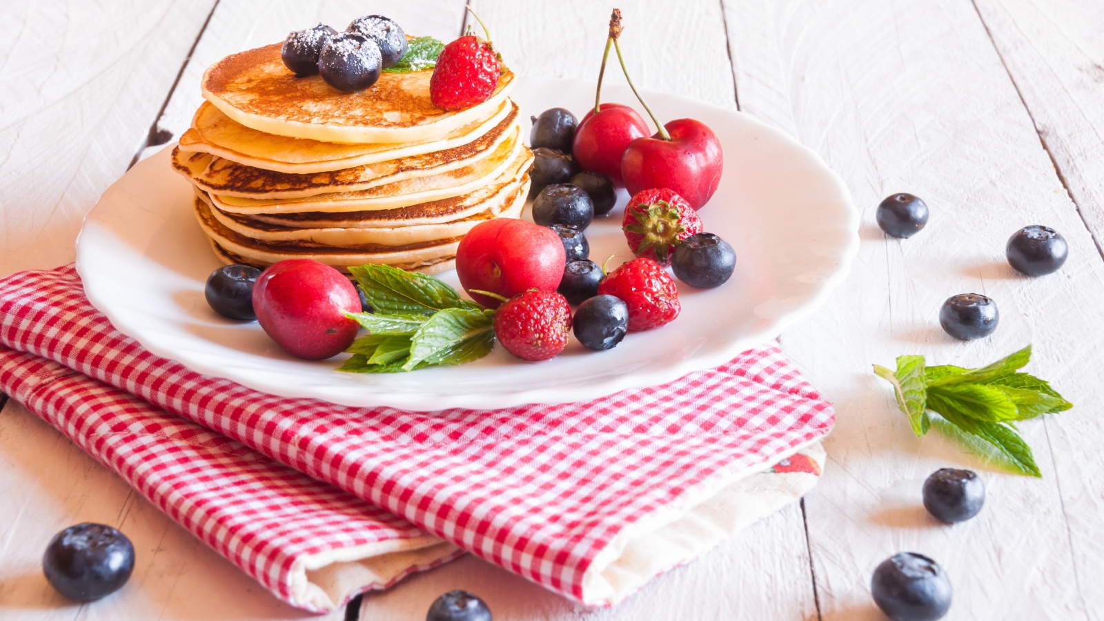 Оладья на белой тарелке с ягодами черники, черешни и клубники