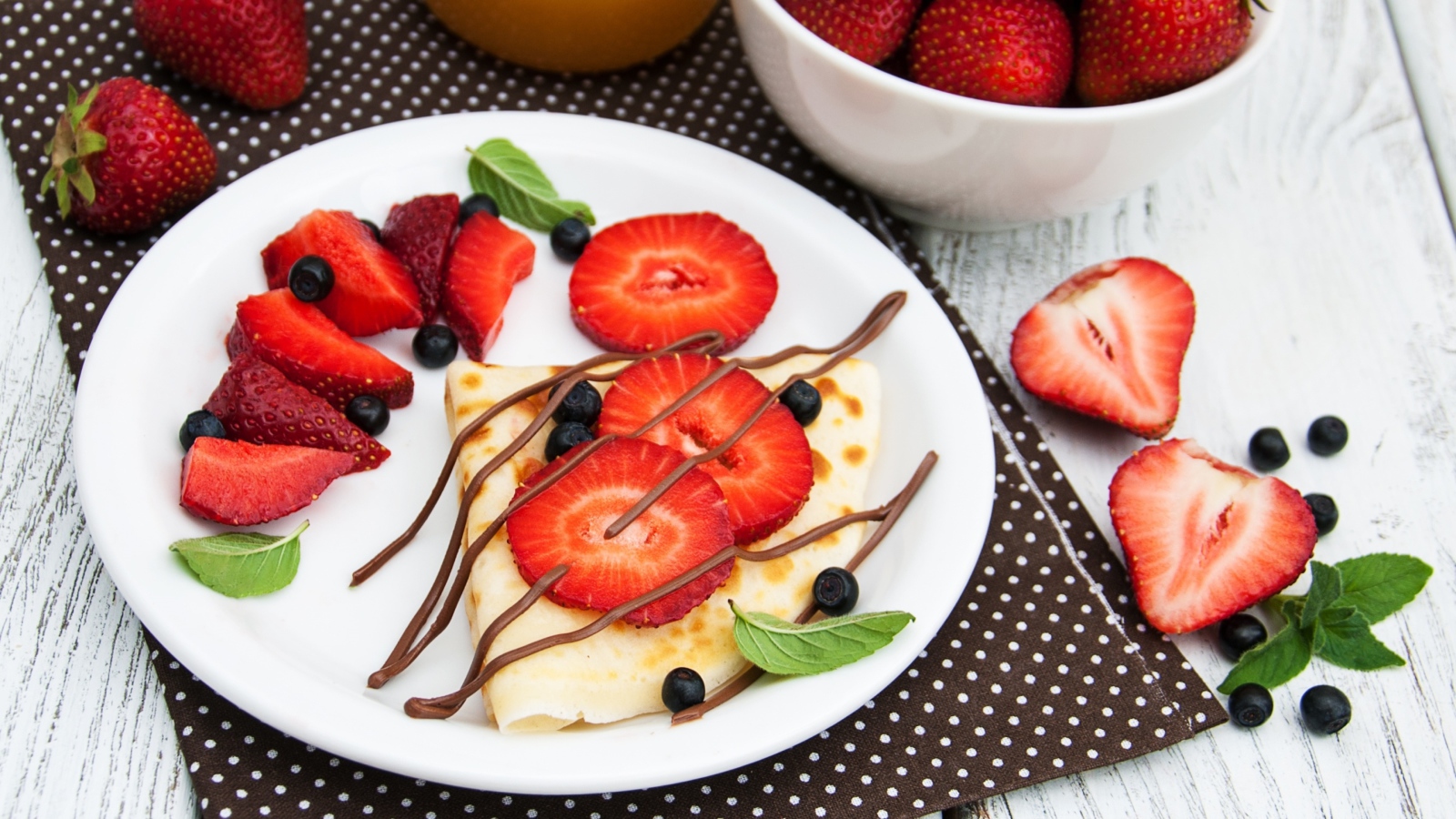 Тонкий блинчик на тарелке с шоколадом, ягодами клубники и черники
